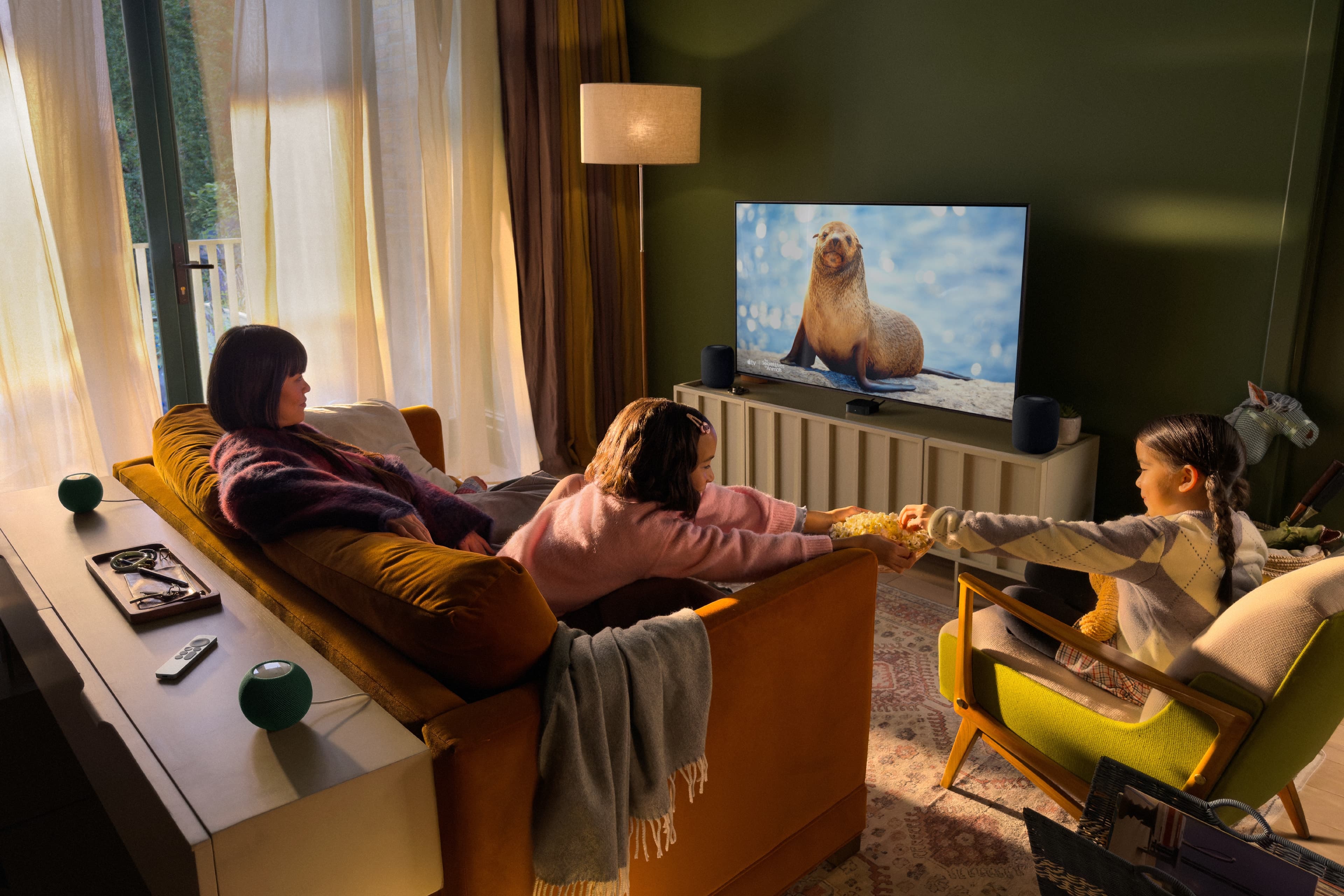 Familie ser på TV med Apple TV 4K, to HomePod og to HomePod mini 2 i et surroundoppsett.