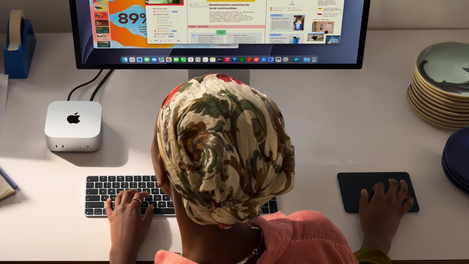 En person arbeider ved en skjerm med en Mac mini på skrivebordet.