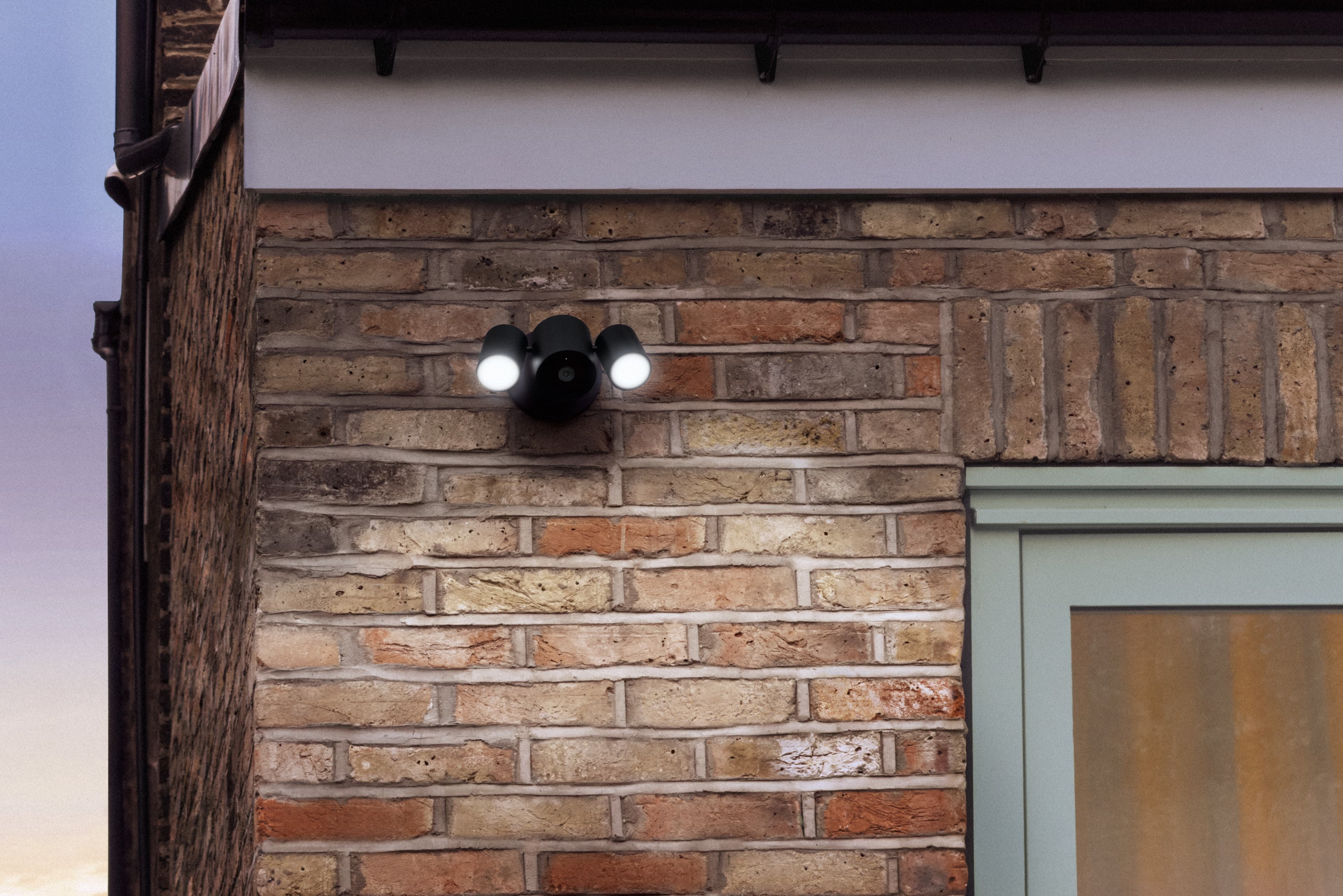 LG Floodlight Cam med to tente lyskastere på en murvegg i skumringen.