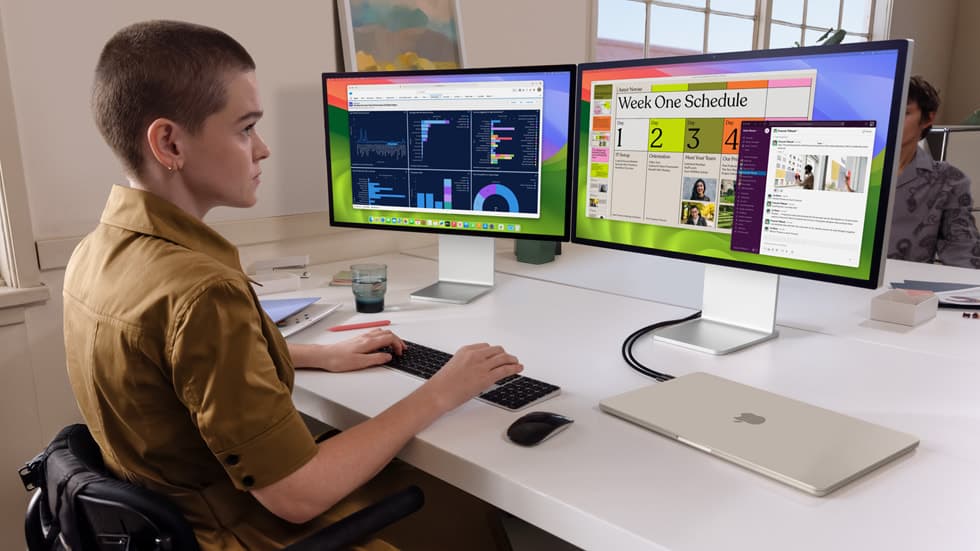 Person ved skrivebord jobber på en MacBook Air koblet til to eksterne skjermer i en flerskjerm-rigg