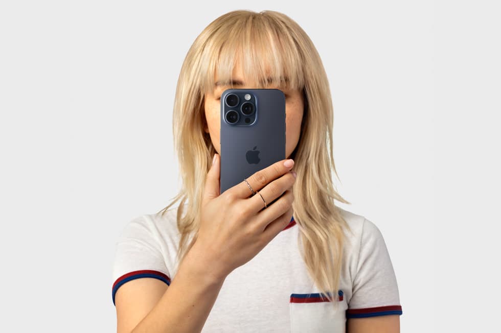En person holder en iPhone 15 Pro foran ansiktet med Apple-logoen synlig, som symbol på personvern og sikkerhet