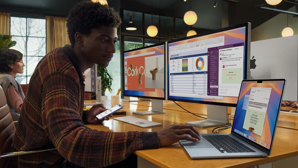 Person jobber med kontordokumenter på en MacBook Air koblet til eksterne skjermer som viser regneark og presentasjoner