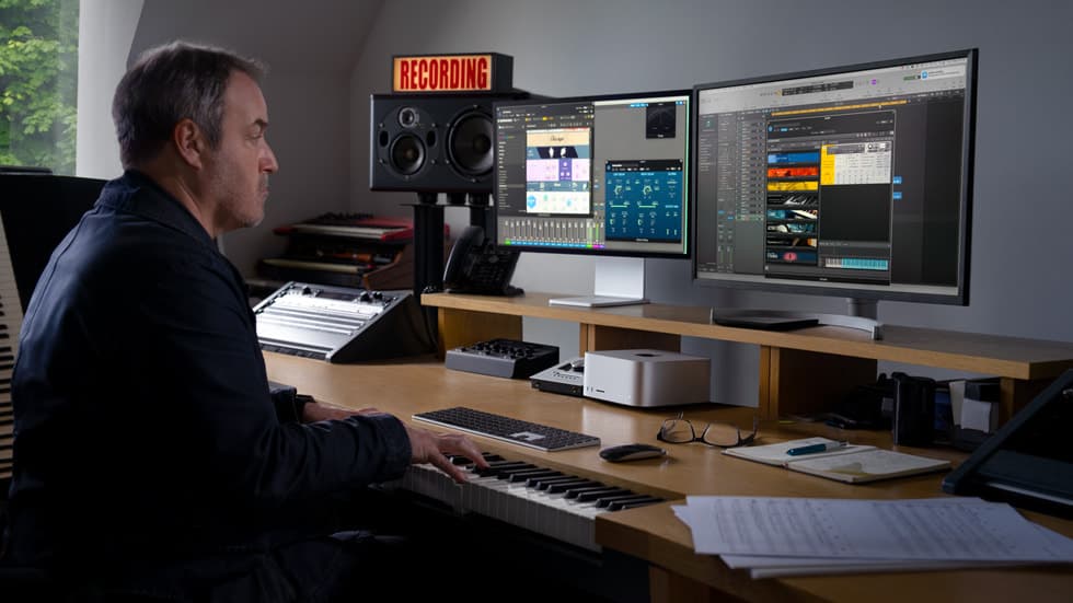 En person jobber ved en Mac Studio i et musikkproduksjonsstudio med to skjermer og lydutstyr