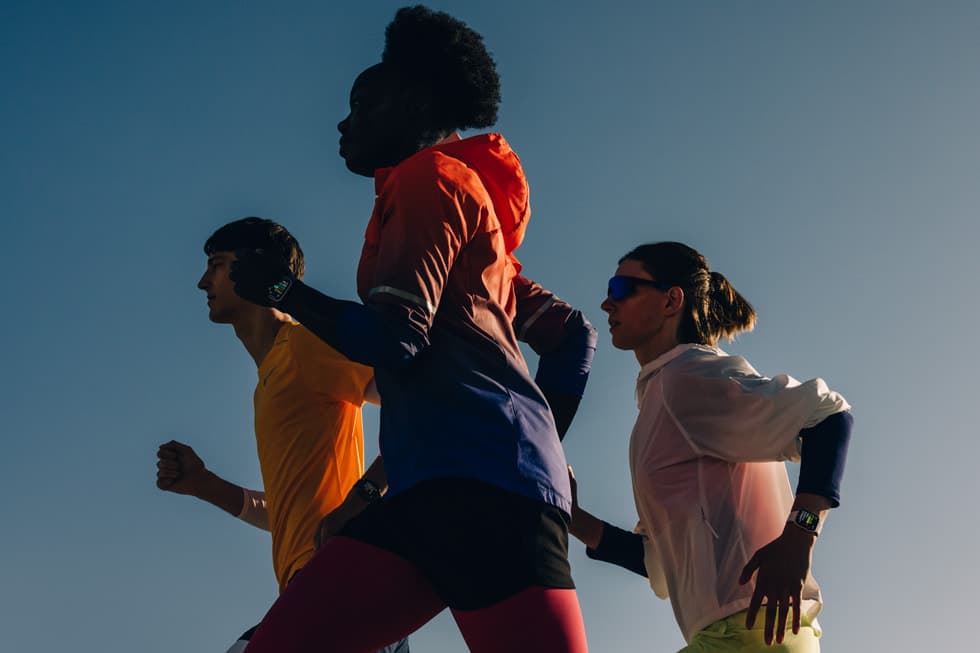 Tre lopere i sportstoy bruker Apple Watch Series 11 under en treningsokt mot bla himmel