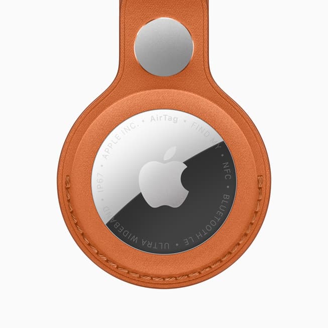 En AirTag med Apple-logo festet i en oransje FineWoven nøkkelring-holder
