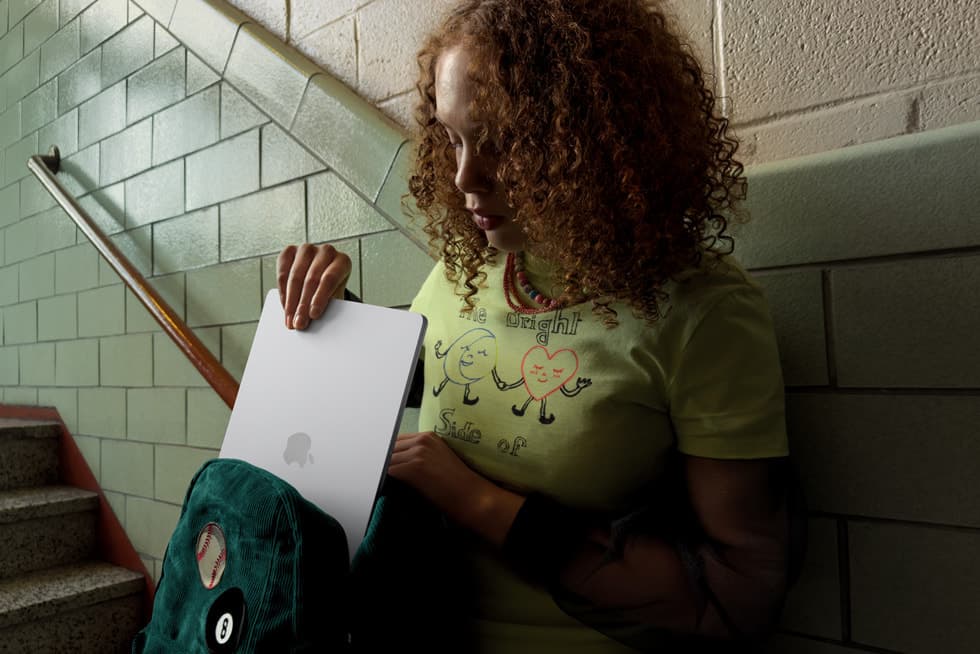 En person bruker en sølvfarget MacBook Air sittende i en trapp