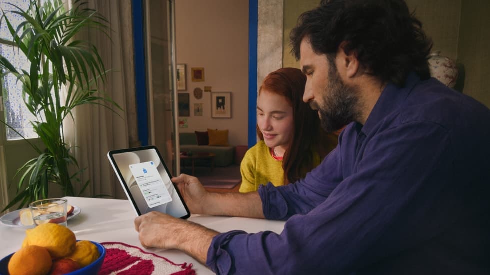 En voksen og et barn sitter sammen ved et trebord og bruker iPad.